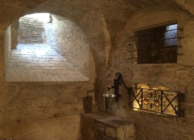 Vista dell'apertura del pozzo Etrusco. Le mura del pozzo sono illuminate da faretti per evidenziarne la struttura e profondità. Alla sinistra del pozzo c'è un piccolo ripiano in muratura con una pompa a leva, un tempo usata per raccogliere l'acqua. L'angolo dove si trova il pozzo è illiuminato dalle finistre incastrate nella volta medioevale.